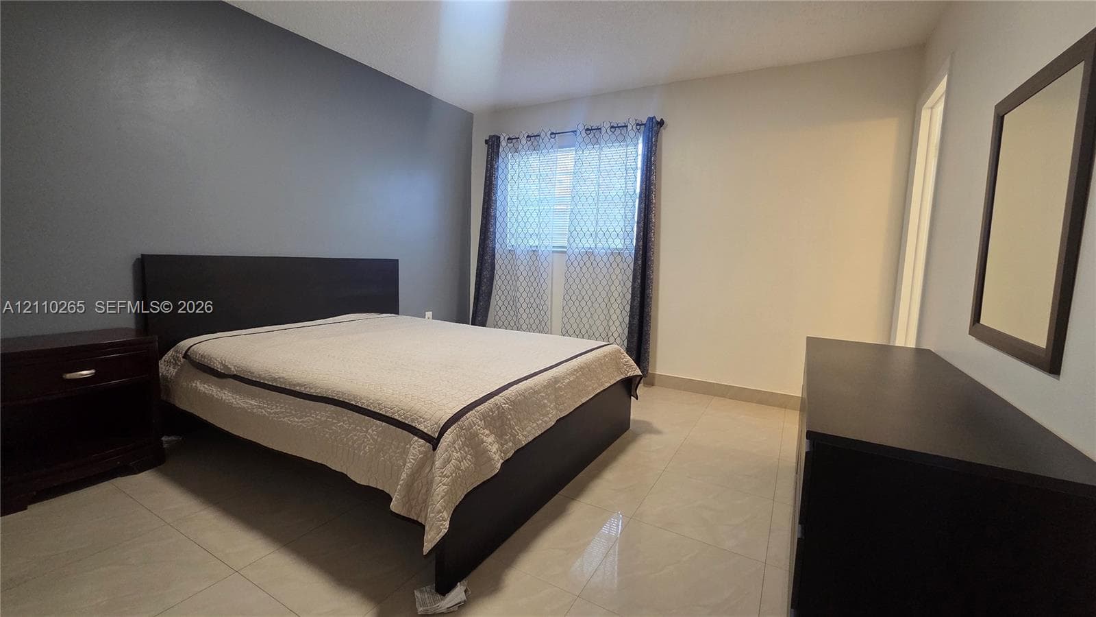 Interior space featuring light-toned tile flooring, neutral wall paint, and a dark-toned accent wall