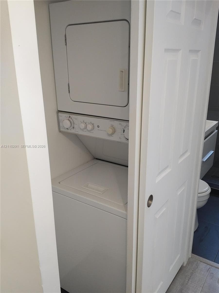 Enclosed laundry closet featuring a stacked washer and dryer unit concealed by a white paneled sliding door