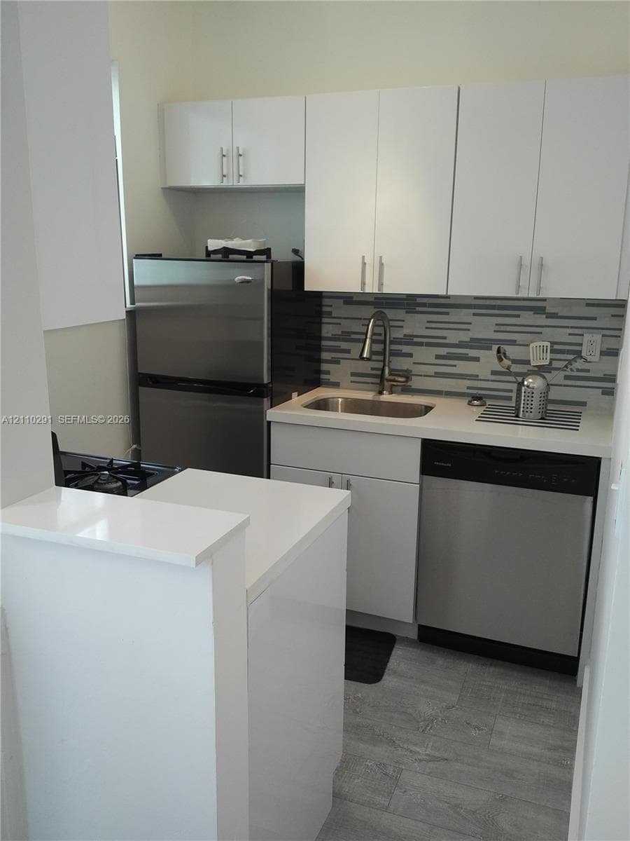 Kitchen featuring white cabinetry, solid surface countertops, stainless steel appliances, multi-toned linear backsplash tile, and wood-finish flooring