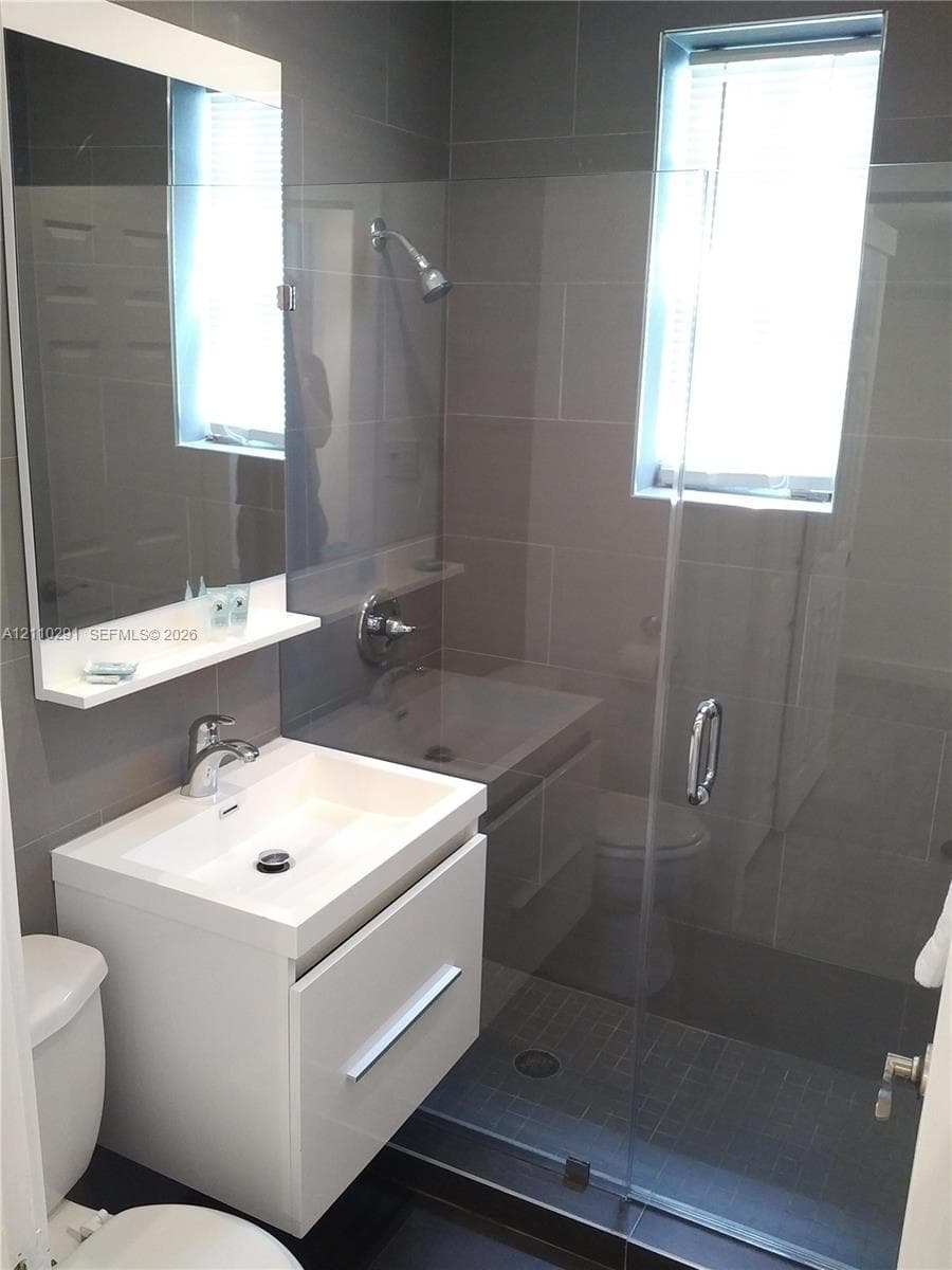 Modern floating vanity with a white basin and integrated storage, frameless glass shower enclosure, floor-to-ceiling tile surround, and wall-mounted mirror with integrated shelving