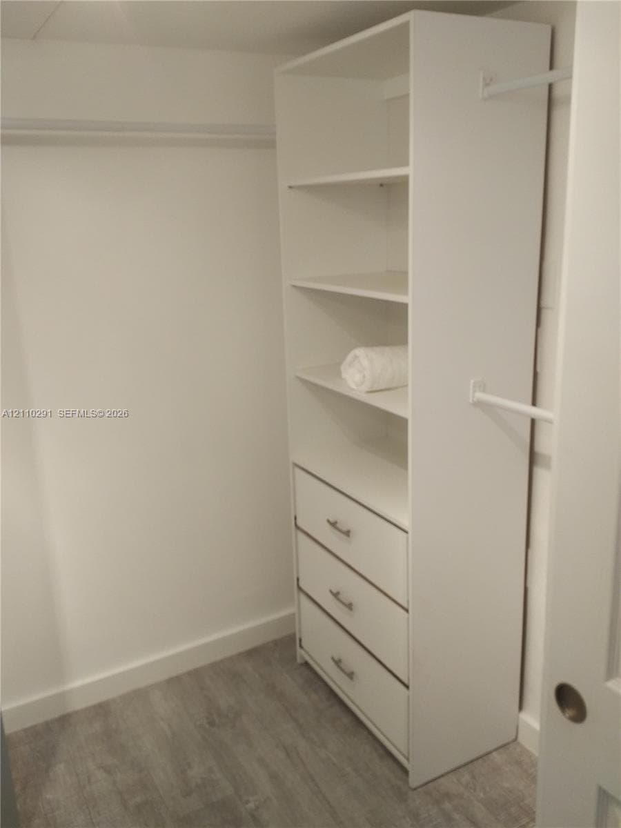 Custom closet organizer featuring white shelving, three built-in drawers with metallic hardware, and white hanging rods, set against wood-finish flooring