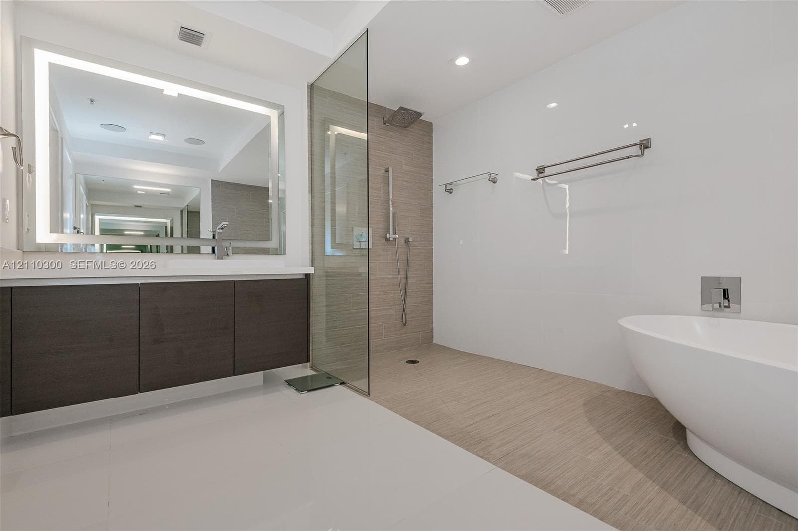 Master Bathroom Freestanding oval soaking tub, wall-mounted faucet, floating wood-finish vanity with a rectangular sink, large format tile flooring, and textured tile accent wall