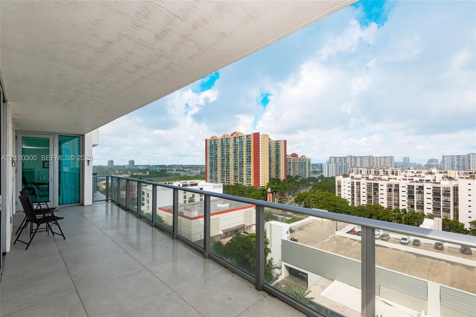 Covered balcony with large-format tile flooring, glass railing system, and floor-to-ceiling sliding glass doors