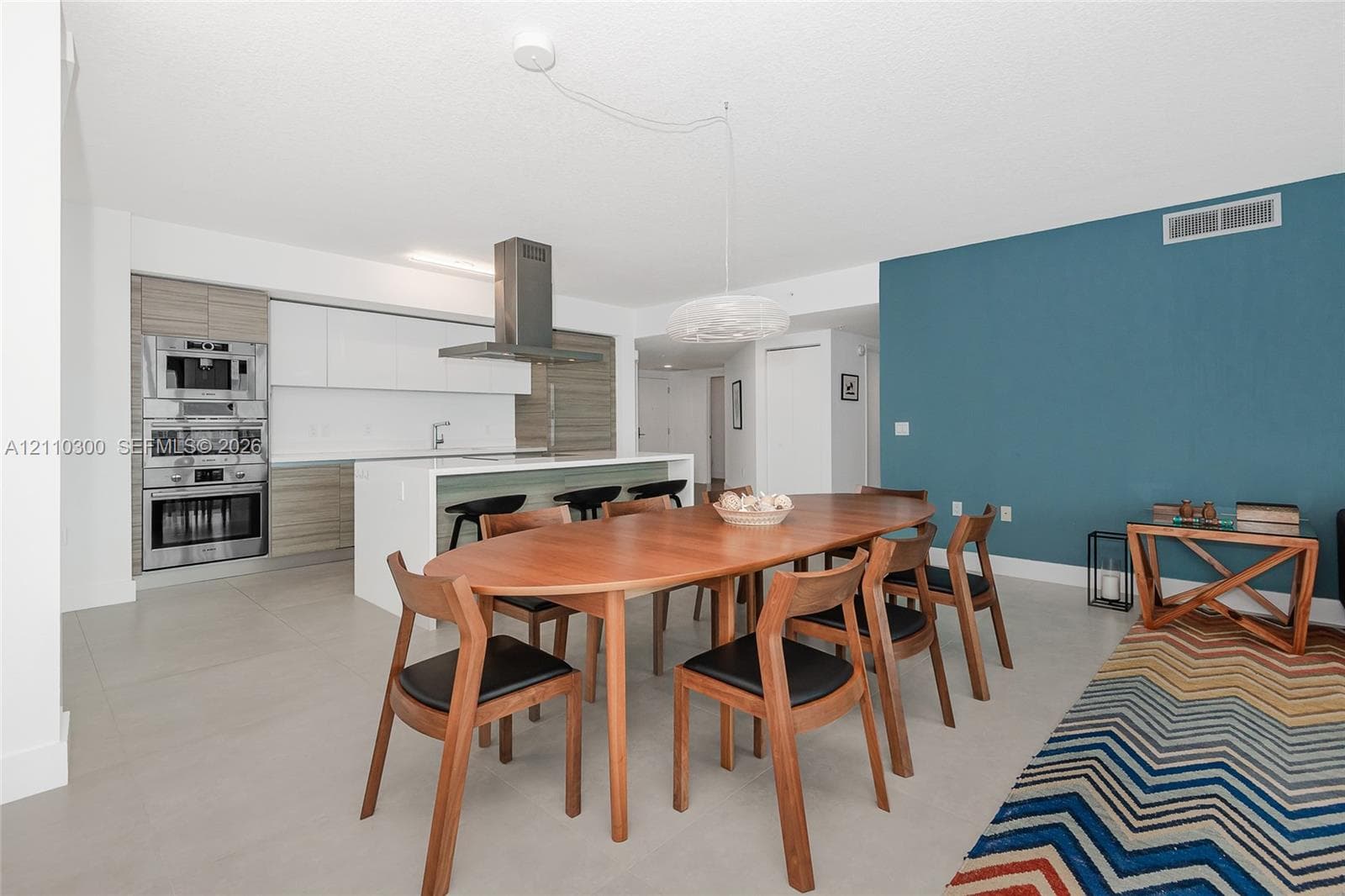 Open-concept living space featuring floor-to-ceiling glass sliding doors, modern cabinetry with a dual-tone finish, built-in stainless steel appliances, a kitchen island with stone-finish countertops, and large-format tile flooring