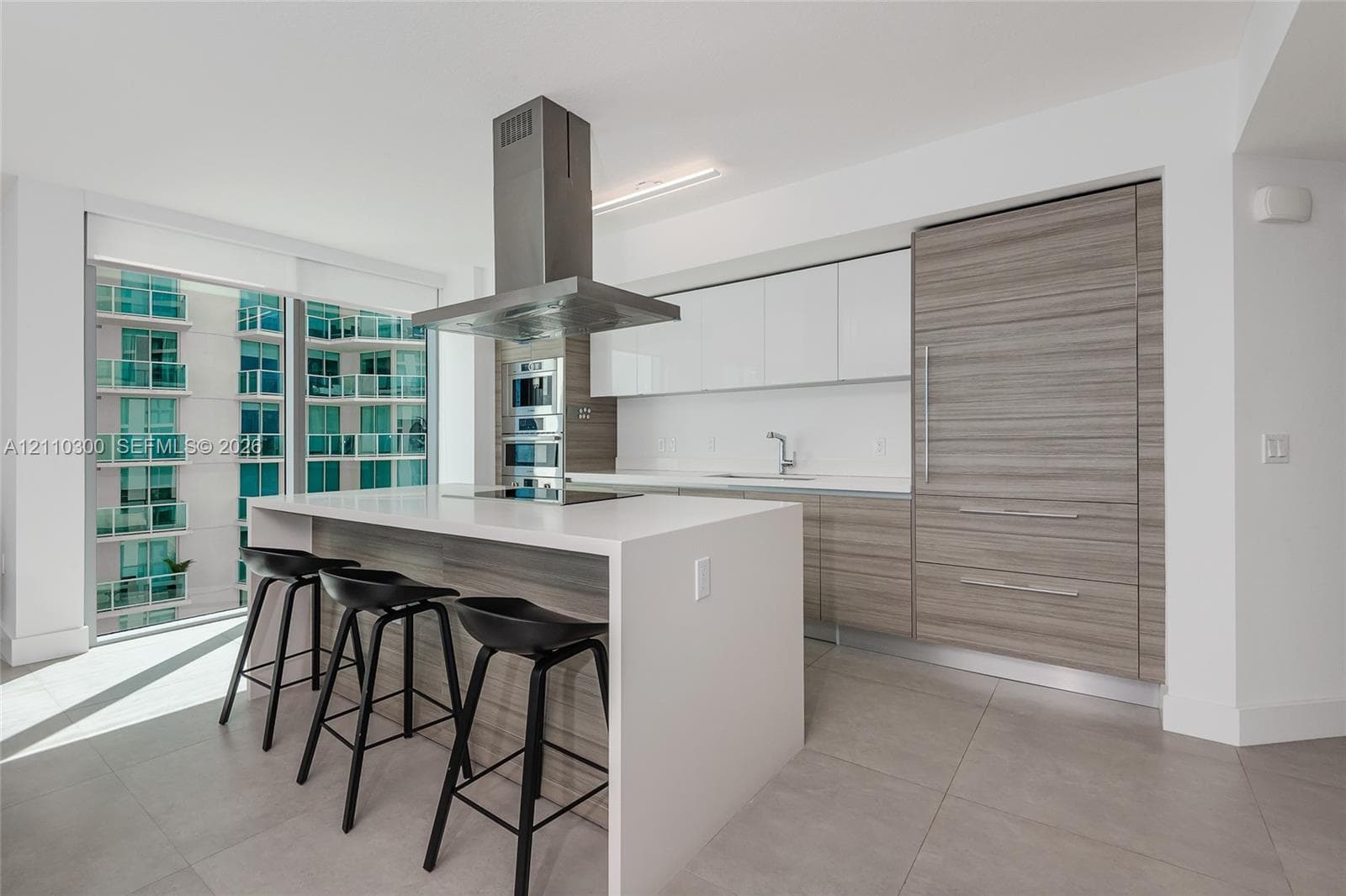 Kitchen featuring a central island with a stone-finish countertop, wood-finish cabinetry, a stainless steel range hood, and tile flooring throughout