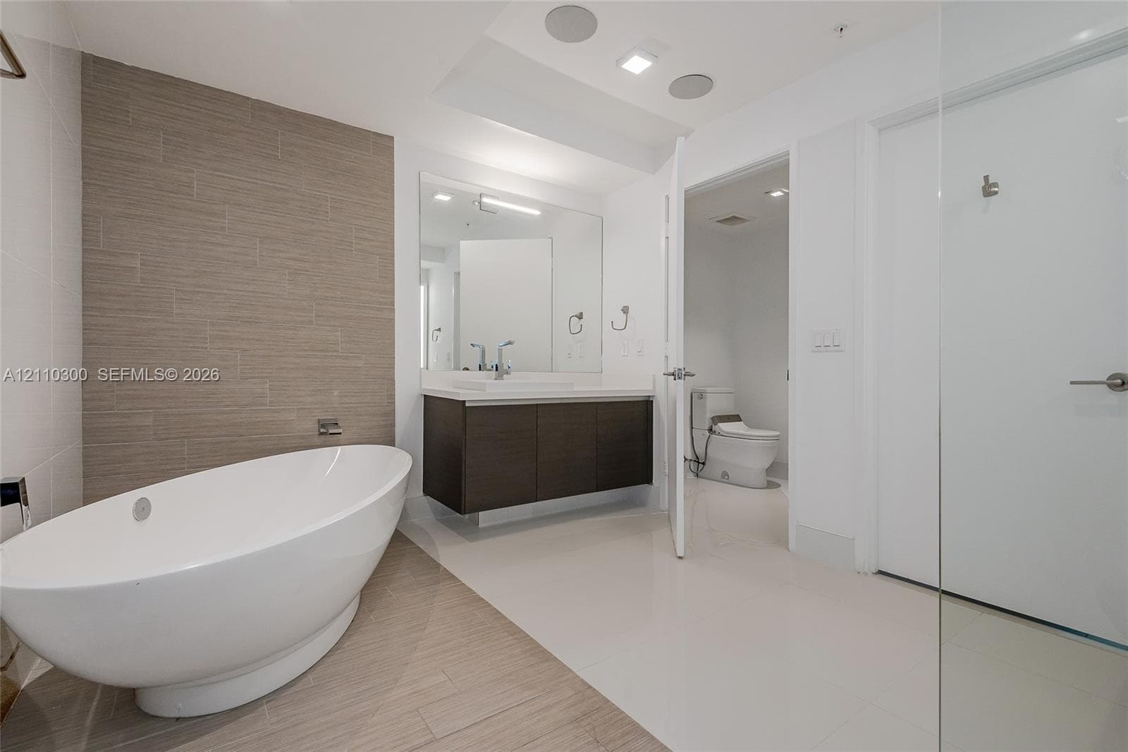 Bedroom 2. Floor-to-ceiling sliding glass door, private balcony, large format tile flooring, and urban skyline backdrop