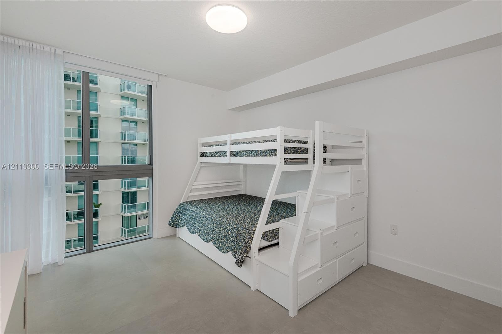 bedroom 3. Floor-to-ceiling windows, neutral tile flooring, and white built-in storage cabinetry with sliding doors and integrated drawers
