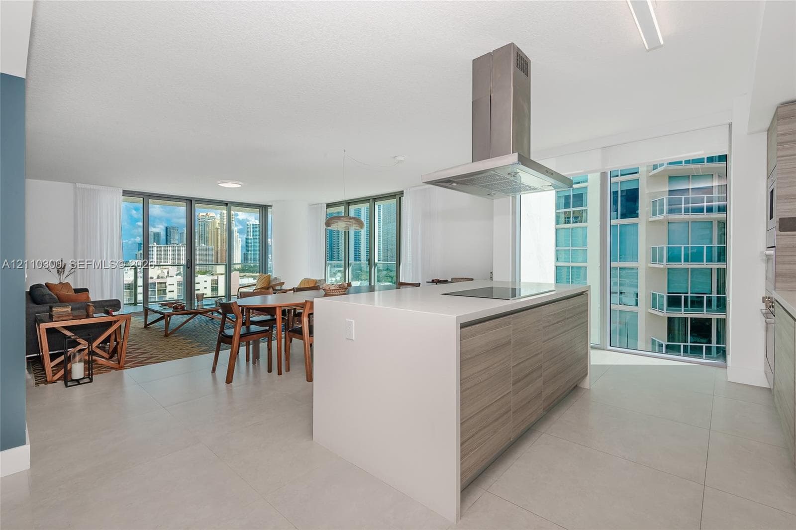 Kitchen featuring horizontal grain wood-finish cabinetry, a central island with a solid surface countertop, stainless steel built-in double ovens, and a stainless steel range hood