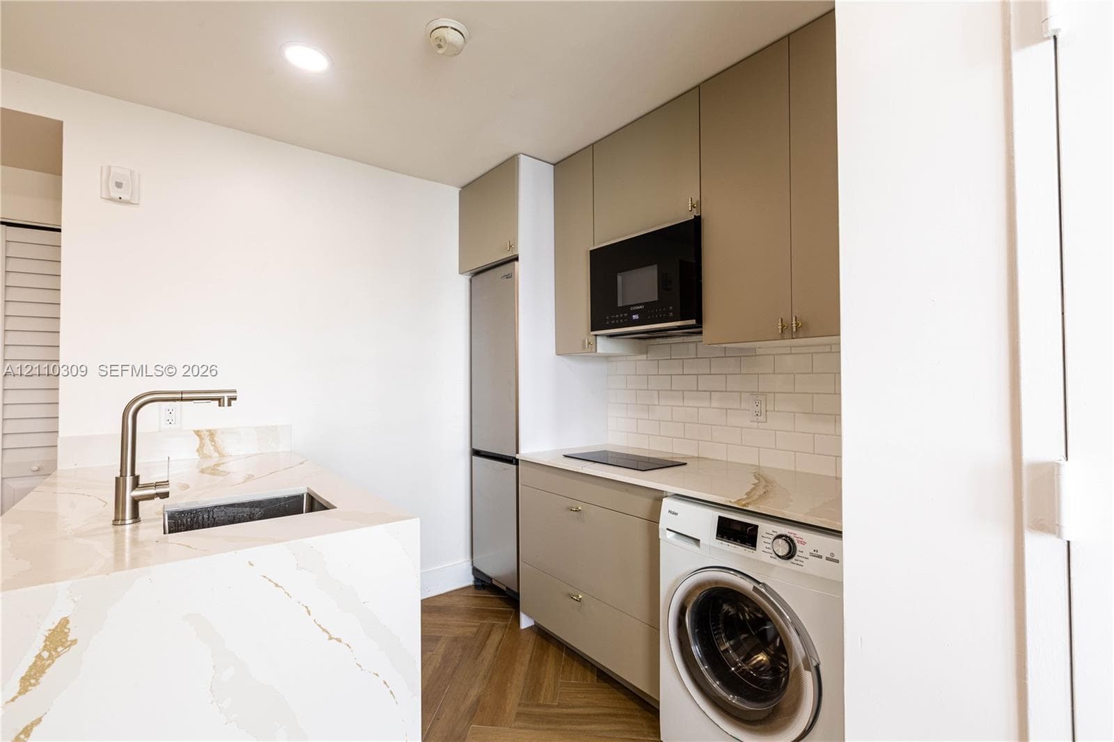 Kitchen featuring stone-finish countertops, herringbone-pattern wood-finish flooring, white subway tile backsplash, flat-panel cabinetry, and integrated laundry appliances
