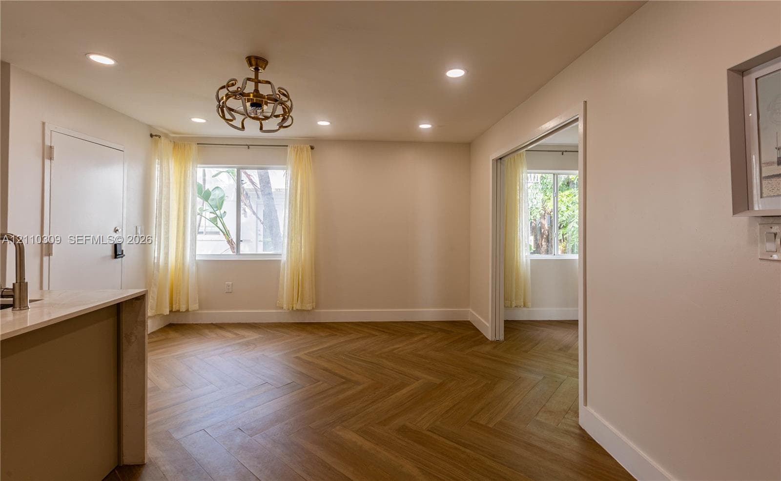Interior space featuring herringbone-pattern wood-finish flooring, recessed lighting, and a metal orb-style chandelier