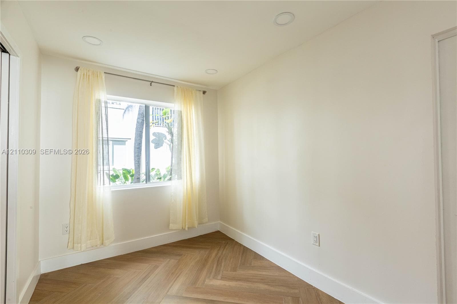 Interior space featuring herringbone-patterned wood-finish flooring, recessed ceiling lighting, and a single-pane window with metal framing