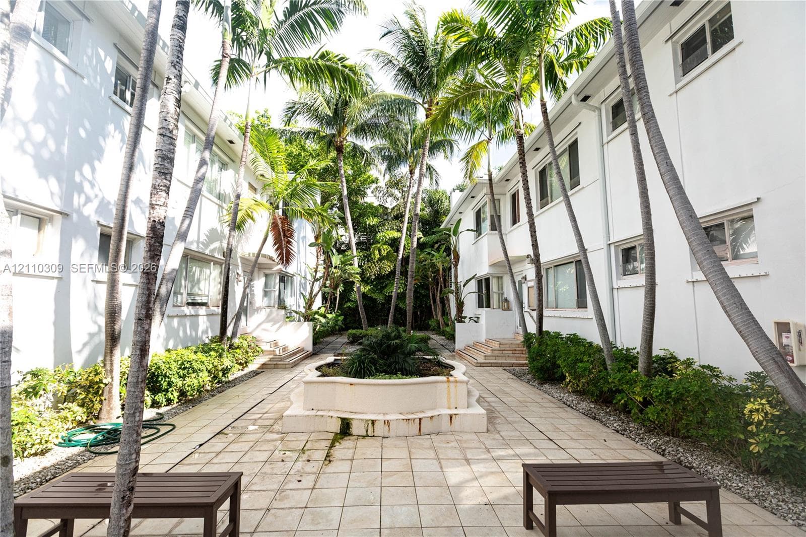 Courtyard featuring stone-tiled flooring, a central concrete planter, multi-level building exteriors, and established palm trees