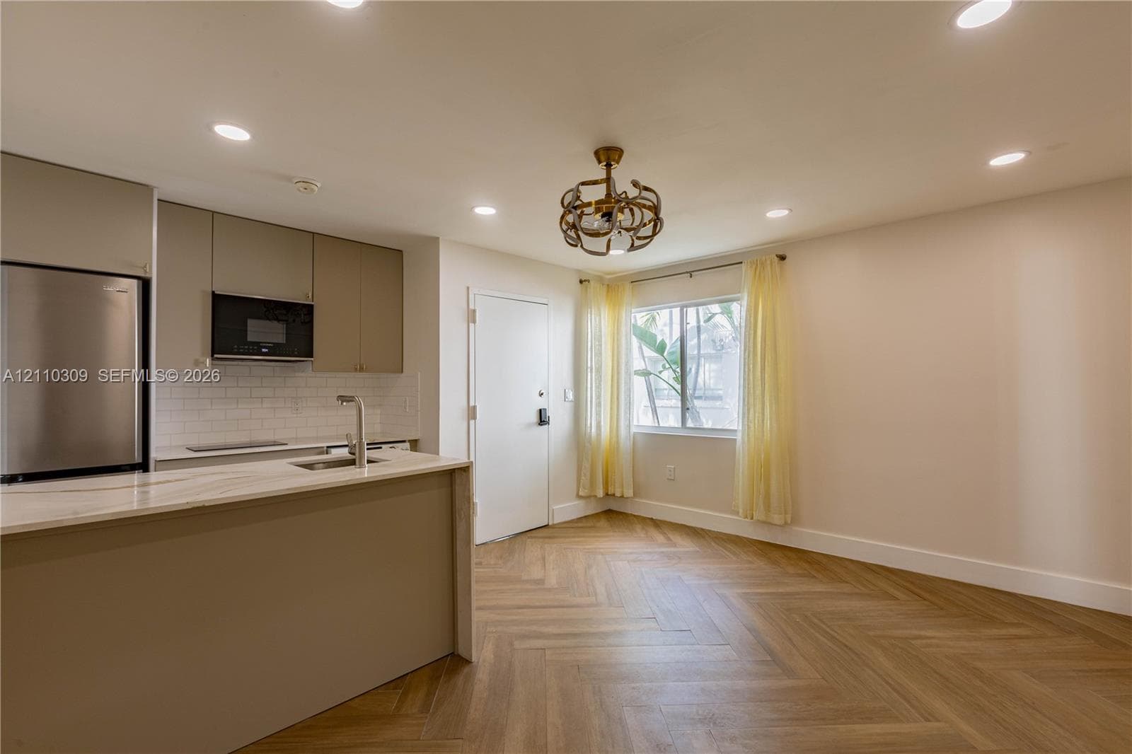 Kitchen featuring flat-panel cabinetry, a stone-surface island, stainless steel appliances, a white subway tile backsplash, and wood-finish herringbone flooring