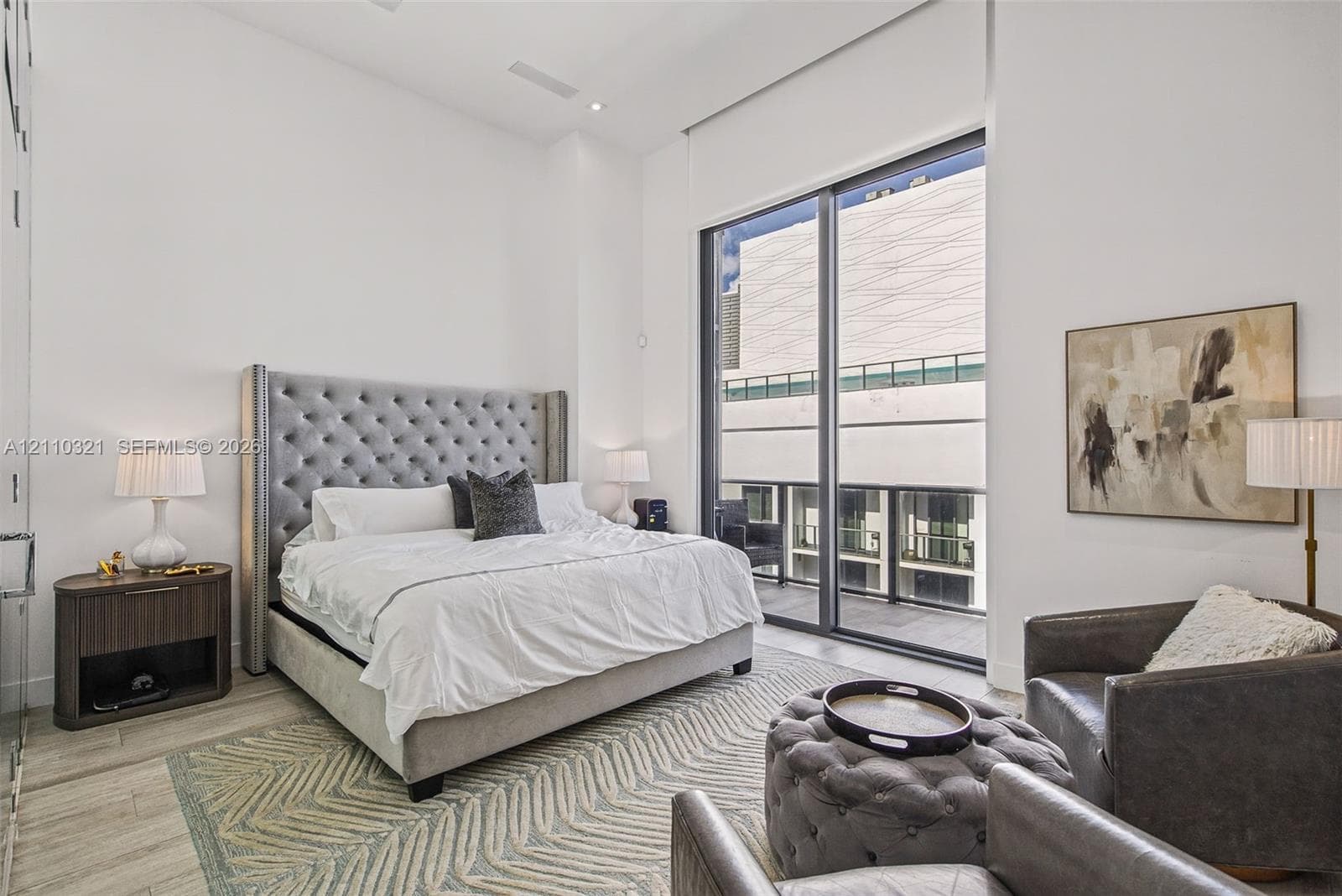 High-ceilinged room with full-height windows, floor-to-ceiling sliding glass door, and wood-finish flooring
