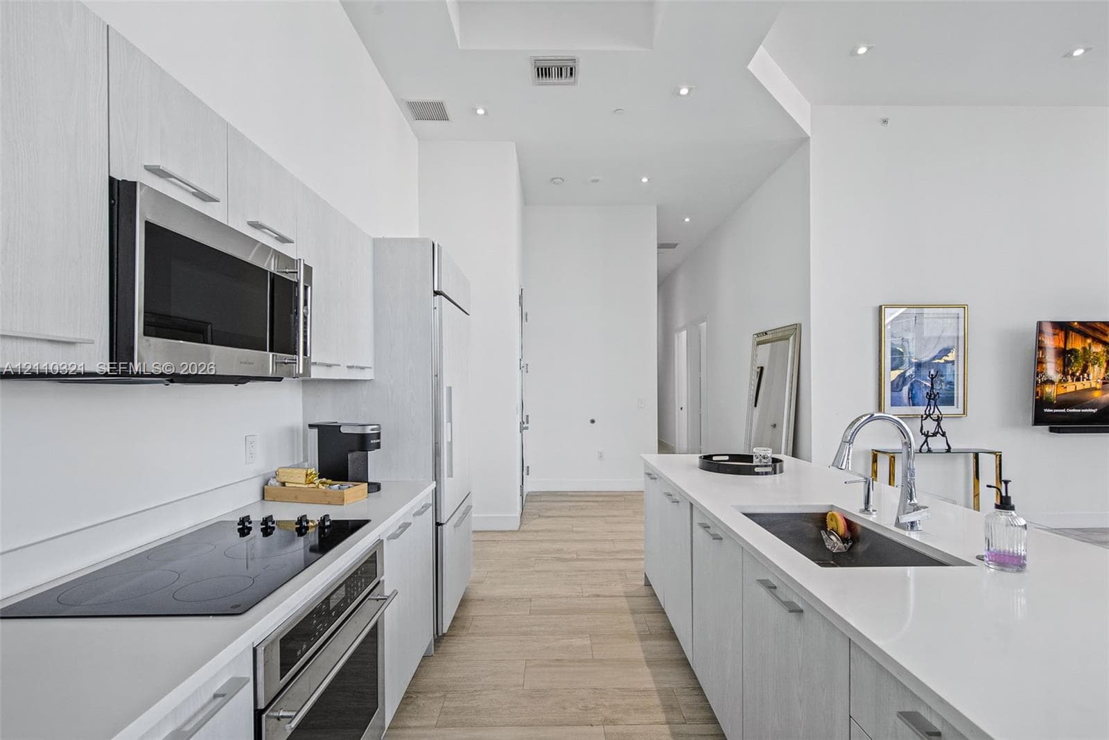 Modern kitchen featuring light-toned cabinetry, stainless steel appliances, a center island with an undermount sink, quartz countertops, and wood-finish flooring
