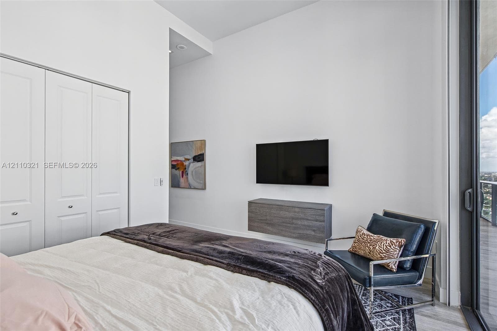 High-ceiling room featuring a wall-mounted floating storage unit, full-height double-door closet with paneled detailing, and a floor-to-ceiling glass sliding door