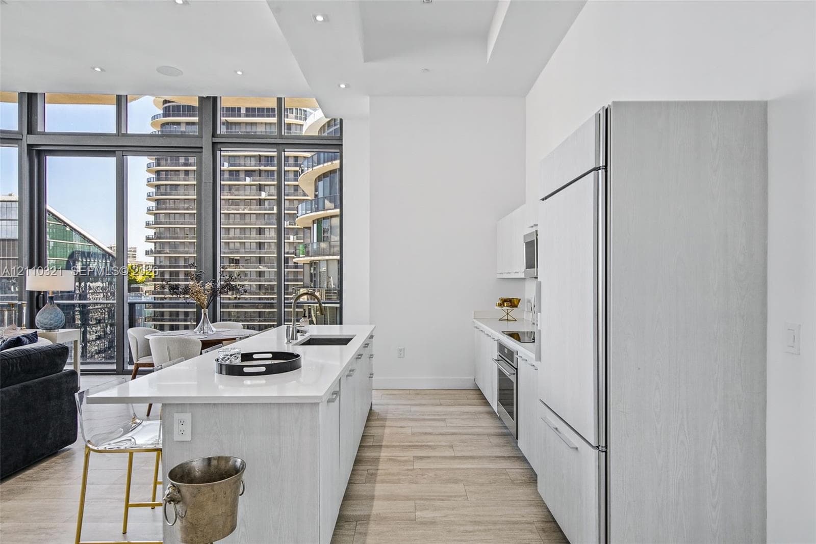 Kitchen featuring floor-to-ceiling windows, white cabinetry with wood-grain finish, center island with stone countertop, stainless steel built-in appliances, and wood-finish flooring