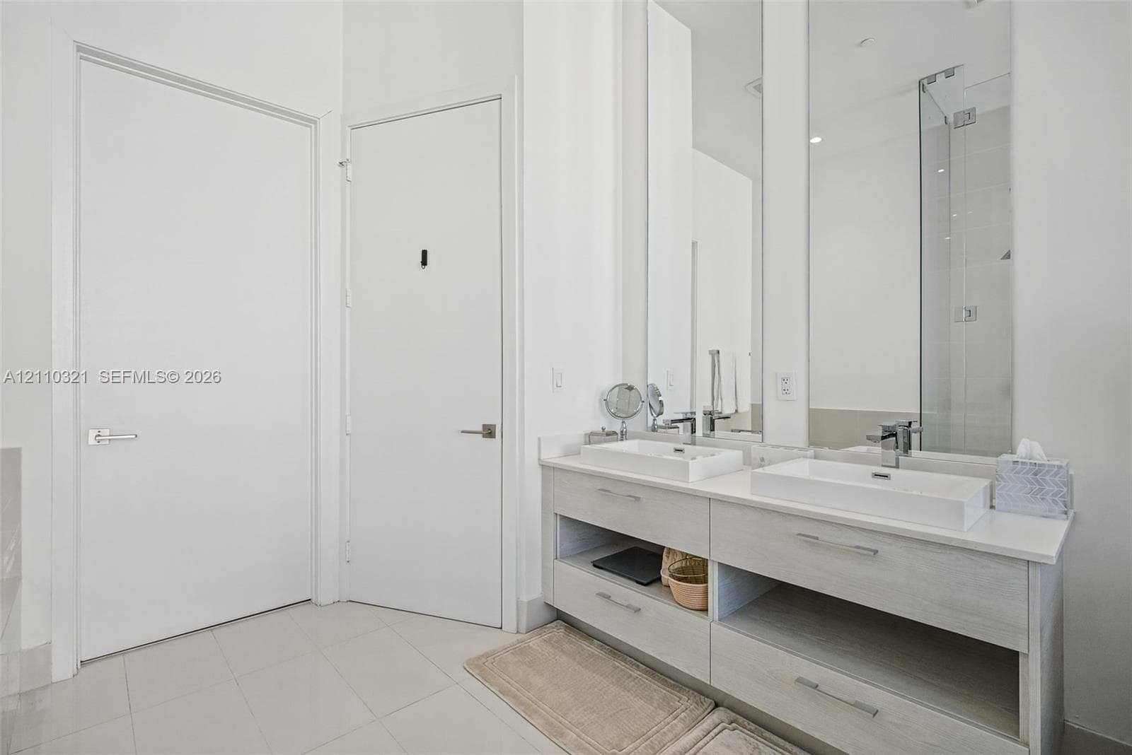 Dual-basin vanity featuring rectangular vessel sinks, light-toned wood-finish cabinetry with open shelving, polished chrome hardware, and large wall-to-wall mirrors