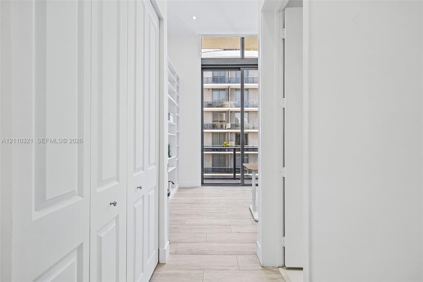 Floor-to-ceiling built-in shelving, wood-finish flooring, sliding glass balcony door, recessed ceiling lighting, and paneled closet doors