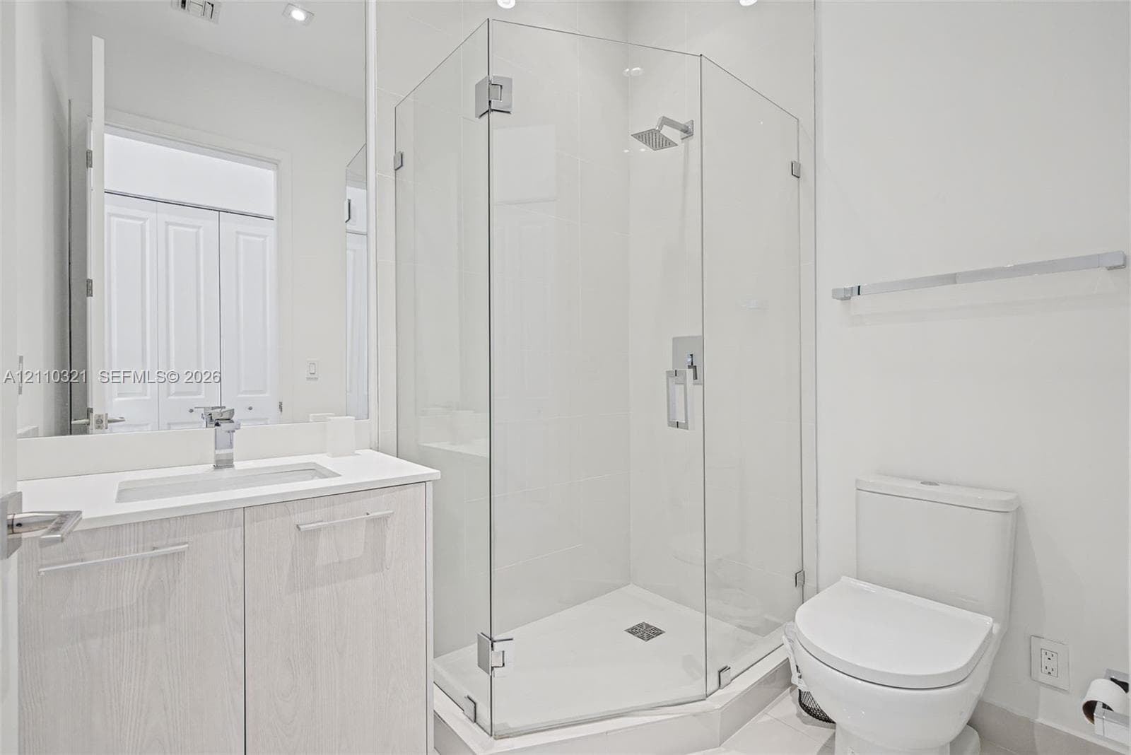 Bathroom featuring a wood-finish vanity with a rectangular sink, quartz countertop, chrome faucet, glass-enclosed shower, and a two-piece toilet