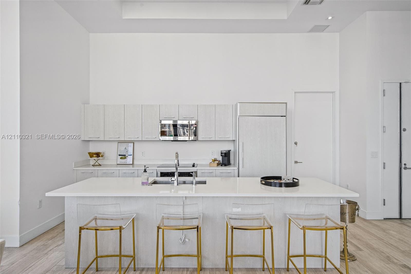 Kitchen featuring light wood-finish cabinetry, a large central island with solid surface countertops, stainless steel appliances, and wood-finish flooring