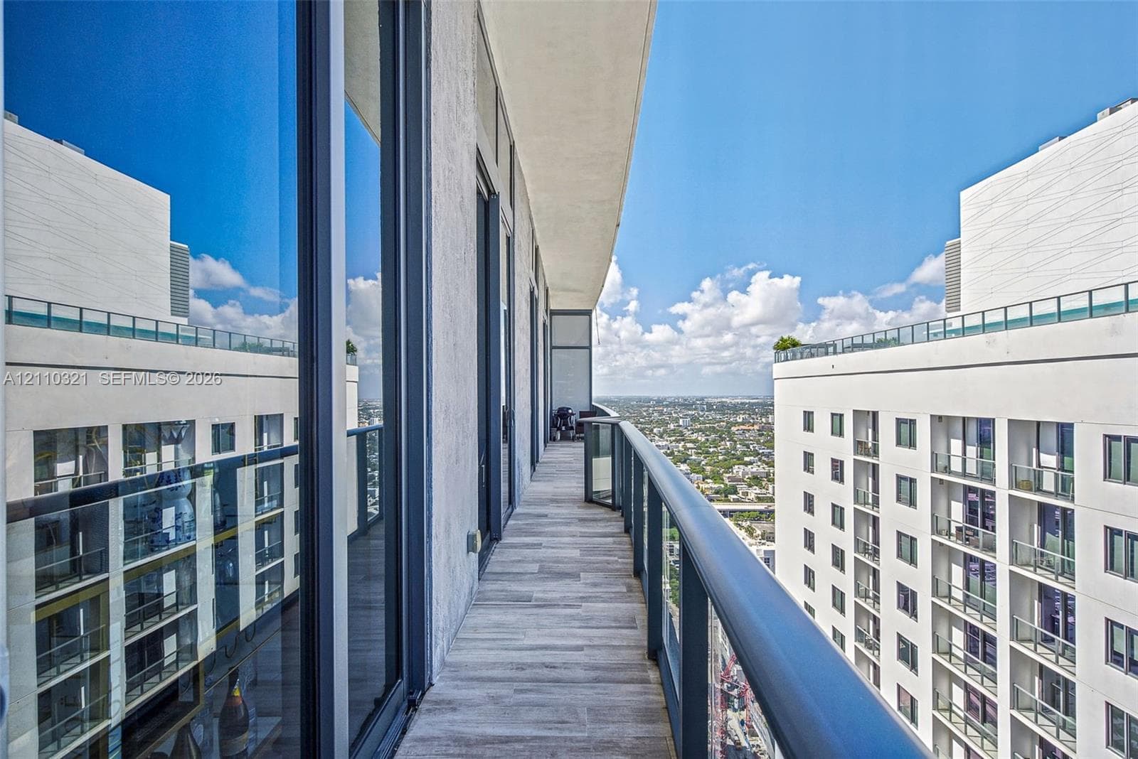 High-rise balcony featuring wood-finish tile flooring, glass panel railings with metal framing, and full-height exterior glass doors