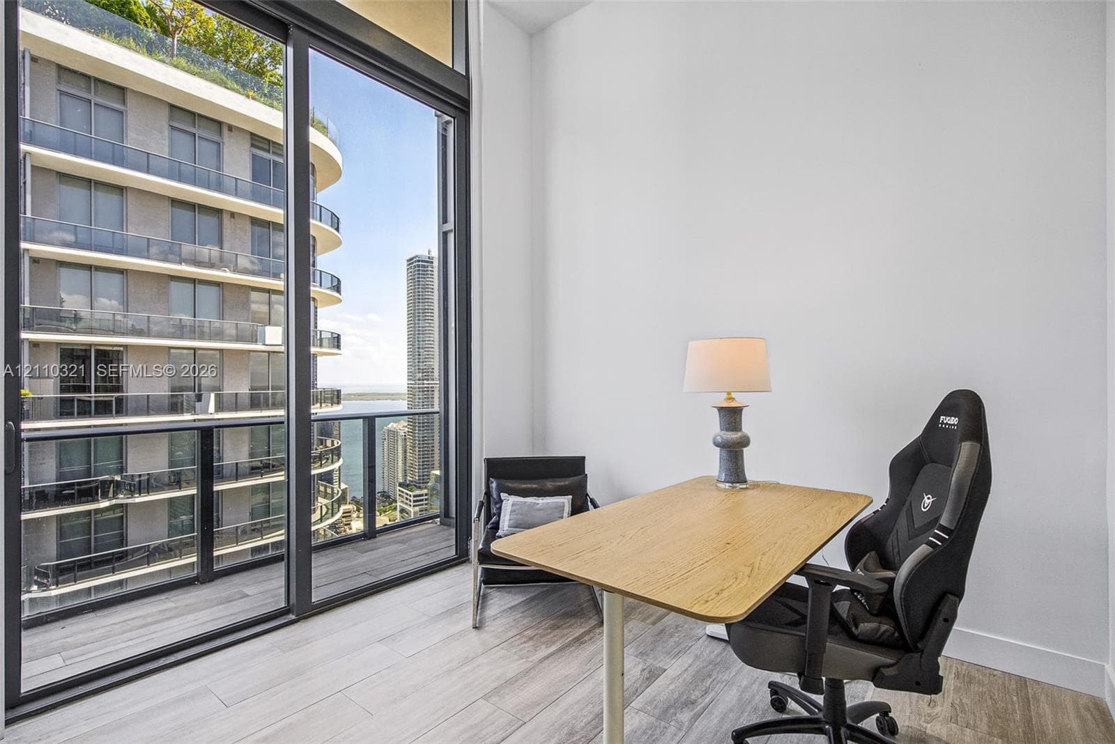 Floor-to-ceiling sliding glass panels, wood-finish flooring, and a private balcony with glass railing