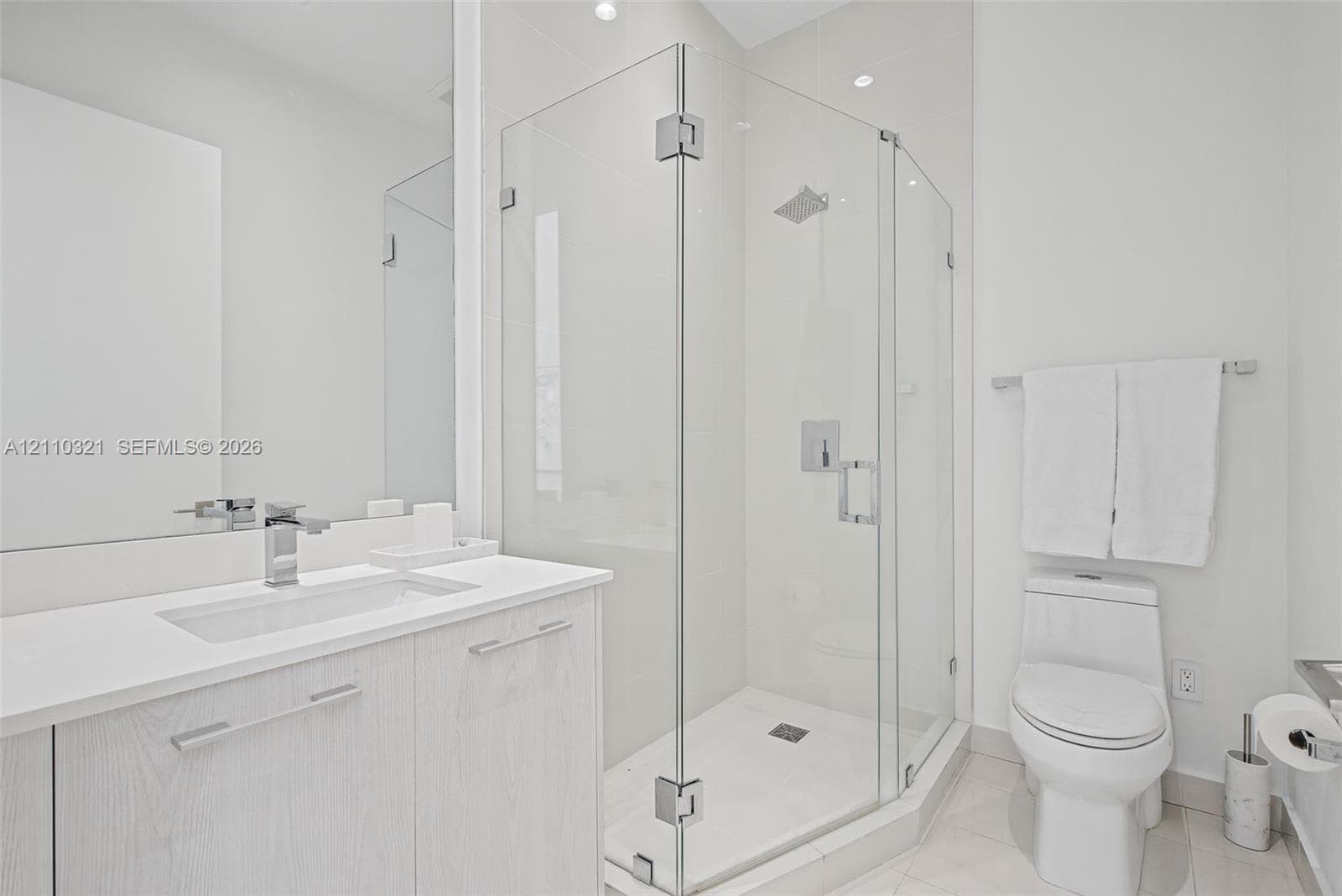 Bathroom featuring a wood-finish vanity with a rectangular undermount sink, stone-surface countertop, walk-in glass-enclosed shower with polished chrome fixtures, and a dual-flush toilet
