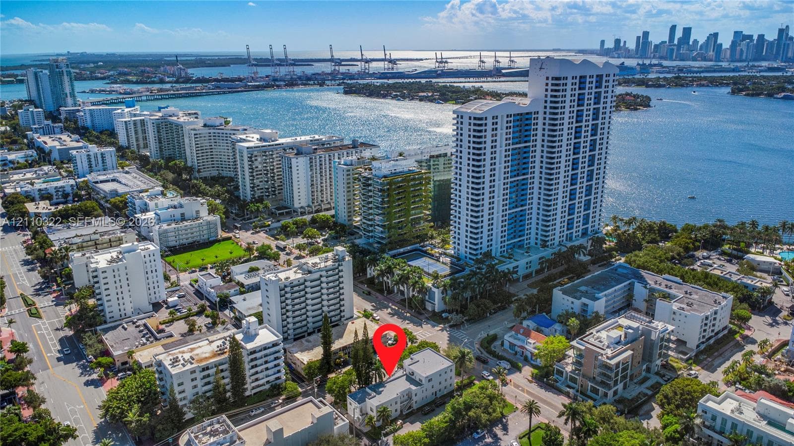 Aerial perspective featuring a low-rise multi-unit residential building with a flat roof, situated in an urban coastal setting with mature trees and proximity to waterfront access