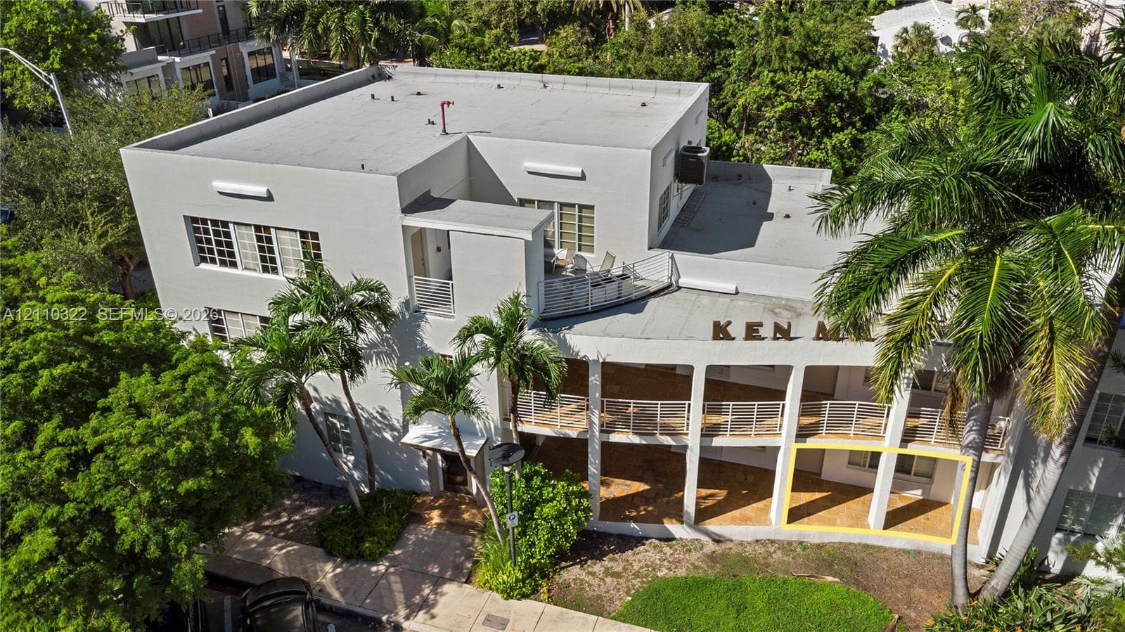 Multi-story building exterior featuring a flat roof, covered ground-level patio, second-story balcony with metal railings, and integrated masonry facade