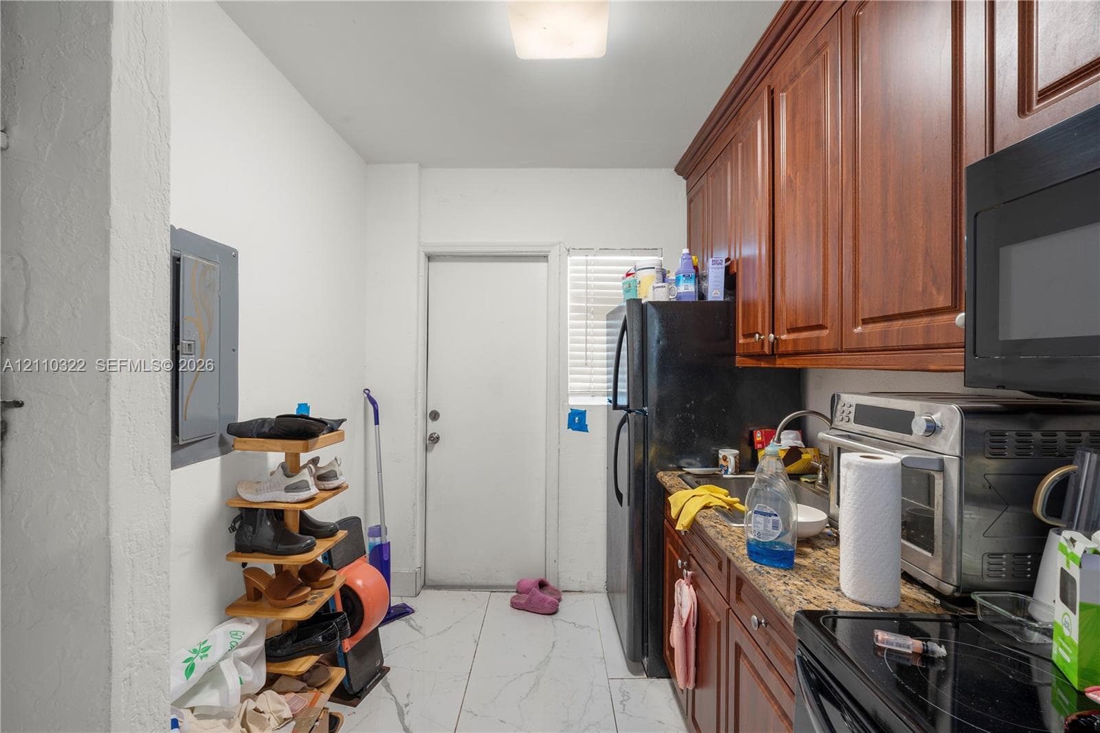 Rich-toned wood cabinetry, stone-finish countertops, stainless steel appliances, and large-format tile flooring