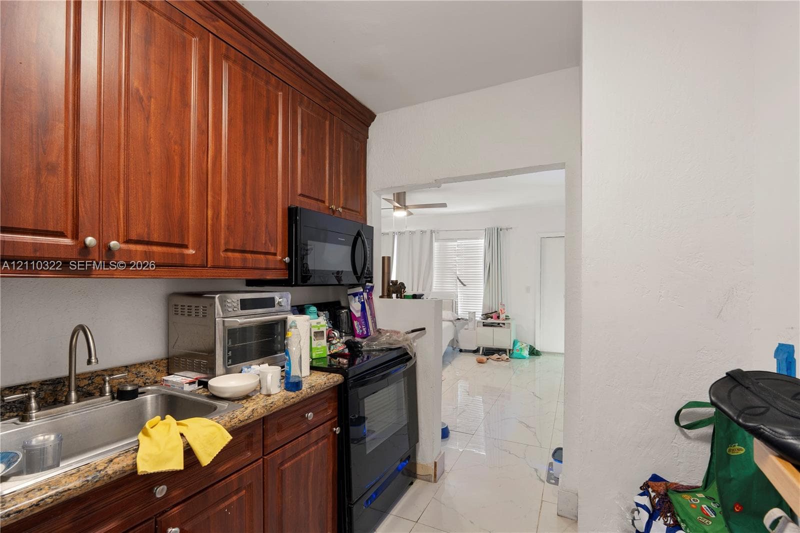 Kitchen featuring stained wood cabinetry, stone-finish countertops, stainless steel sink with gooseneck faucet, and integrated black appliances including a microwave and oven range