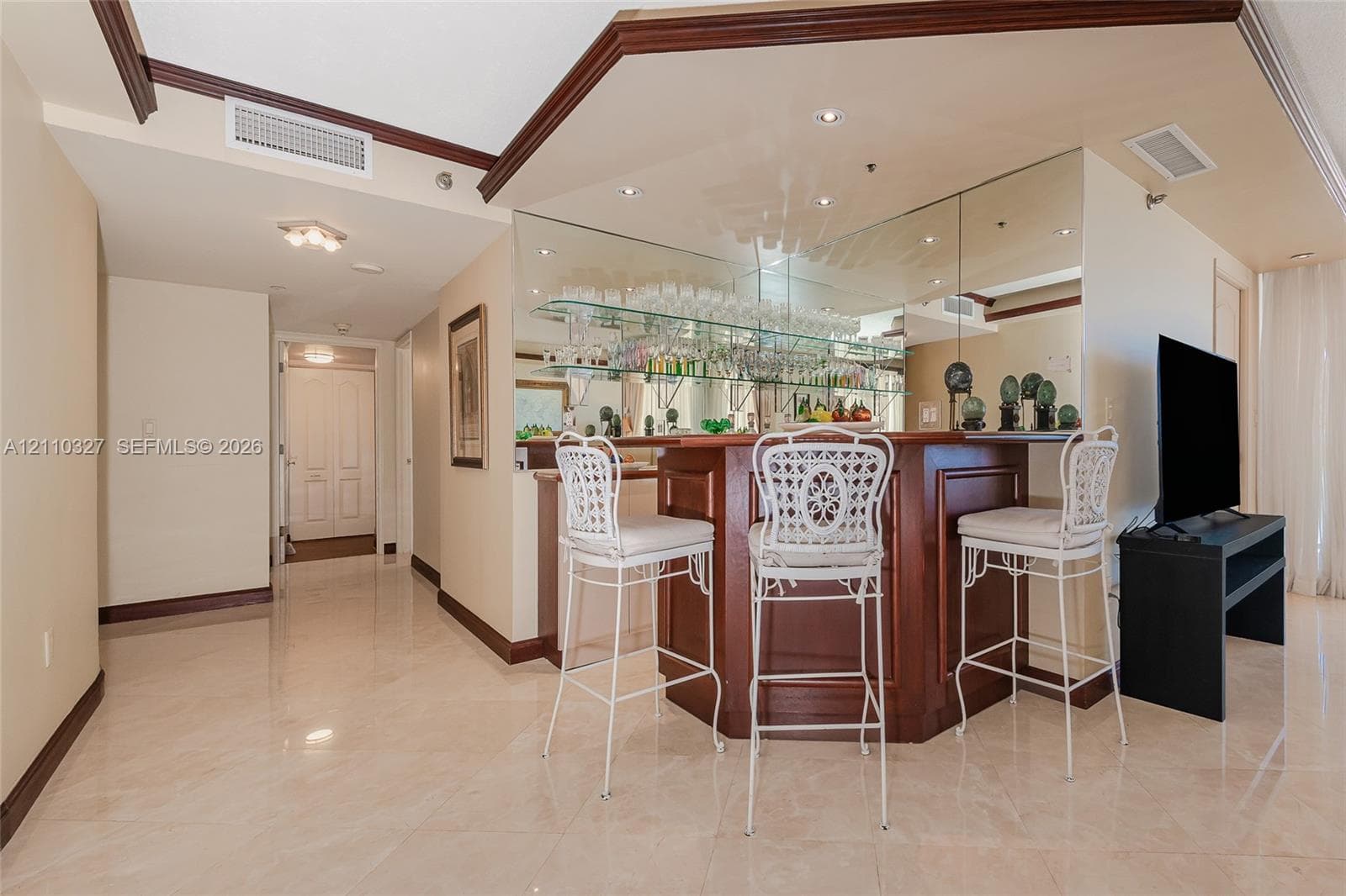Custom wood-finish wet bar with a mirrored backsplash, glass shelving, recessed lighting, and tile flooring