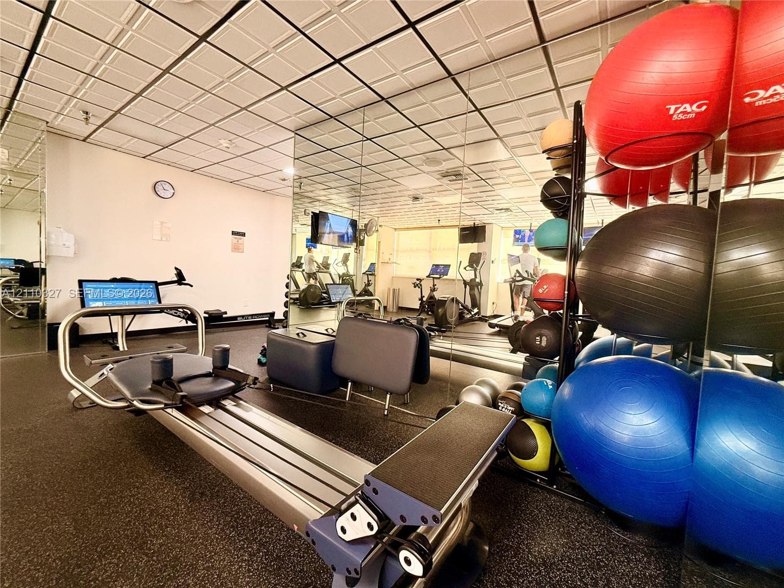 Fitness center featuring rubberized flooring, expansive wall-to-wall mirrors, and a drop ceiling with recessed lighting
