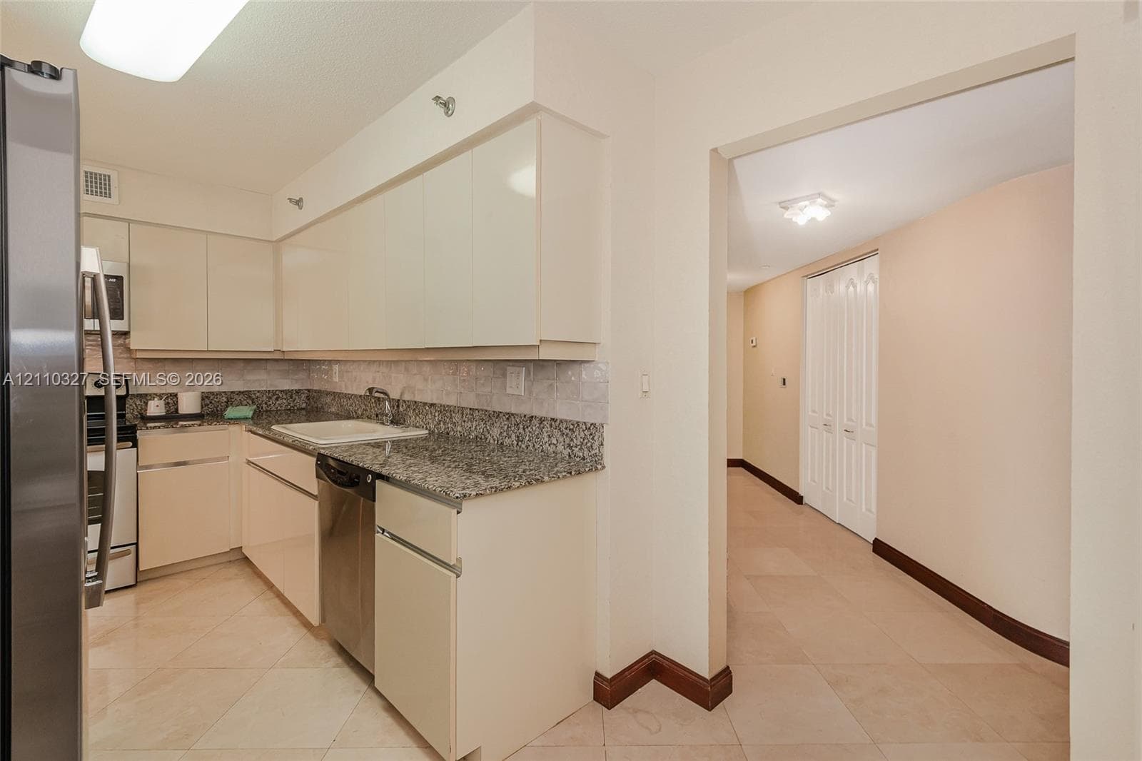 Kitchen featuring light-toned cabinetry, stone-finish countertops, stainless steel appliances, tile backsplash, and tile flooring