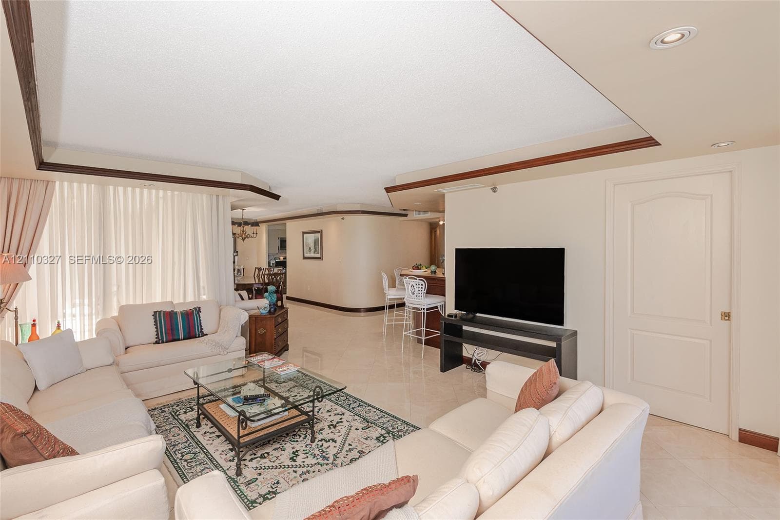 Open-concept interior featuring tray ceilings, neutral tile flooring, built-in breakfast bar, and recessed lighting