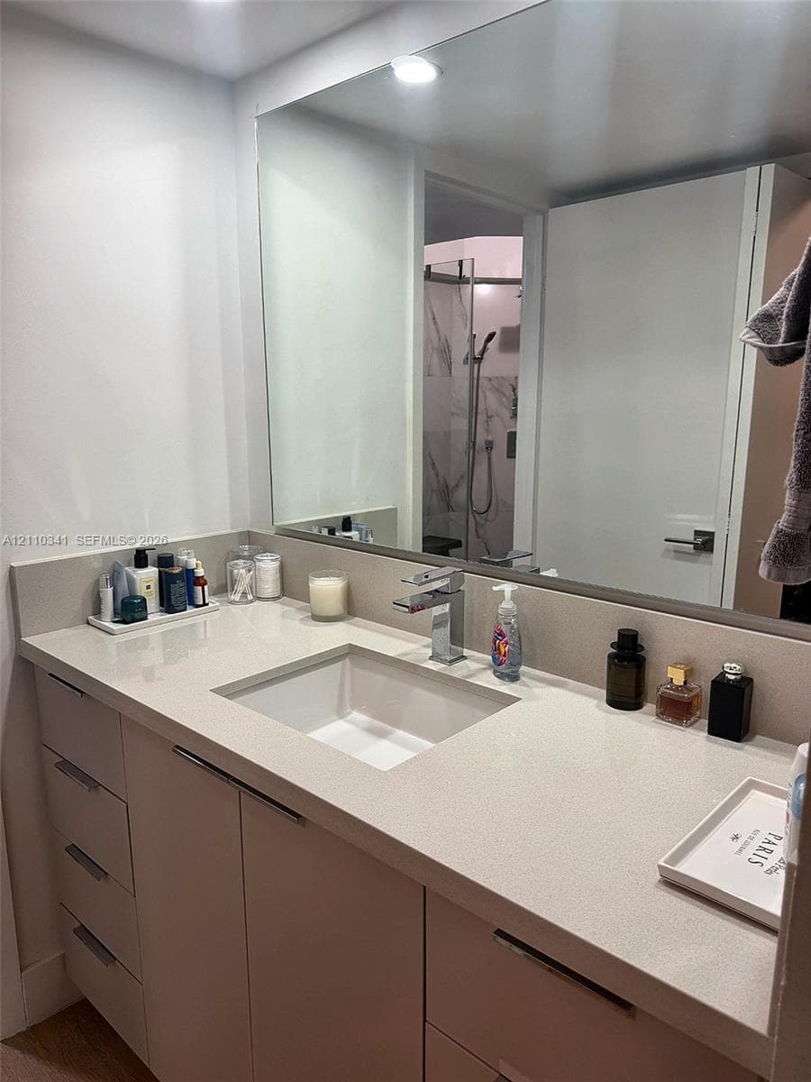 Custom vanity featuring stone-composite countertop, undermount rectangular sink, chrome single-handle faucet, integrated cabinet hardware, and expansive wall-mounted mirror