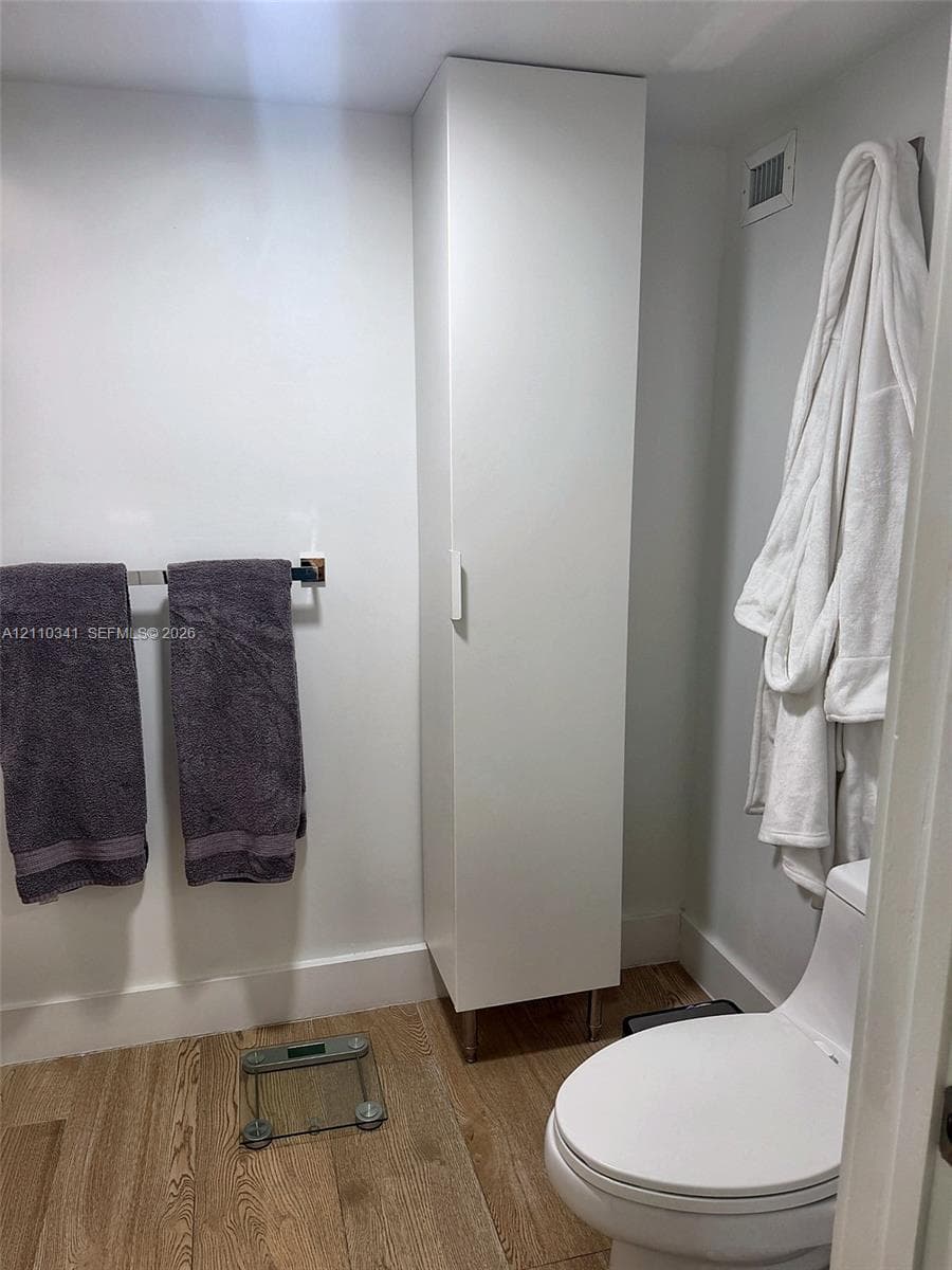 Full-height white storage cabinetry, wood-finish flooring, and a contemporary white toilet