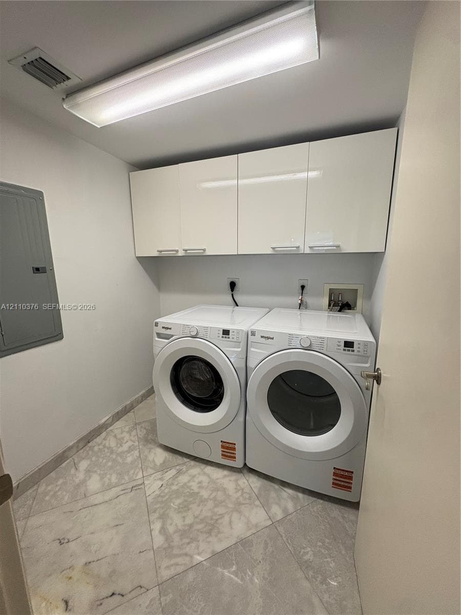 Laundry area featuring high-gloss white upper cabinetry, large-format neutral tile flooring, and integrated laundry hookups