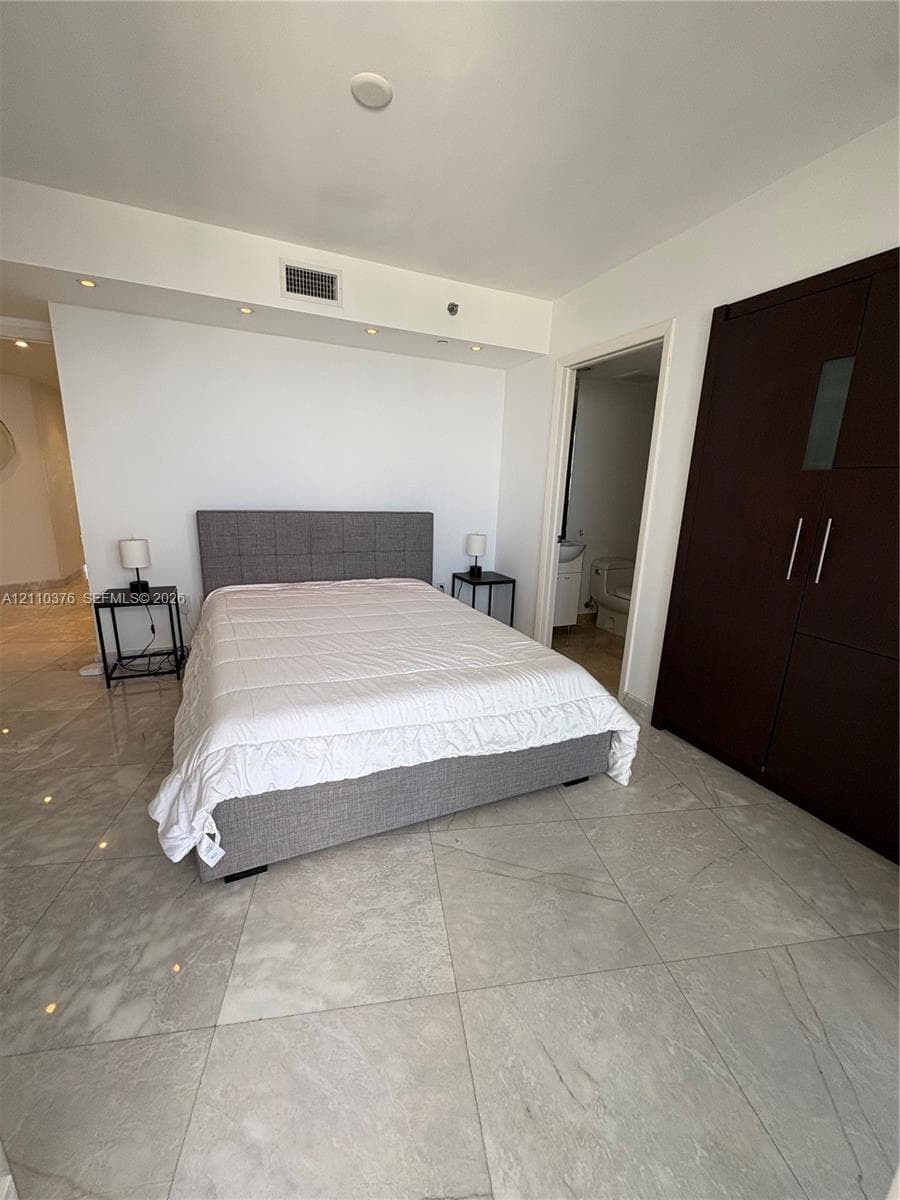 Large-format light-toned tile flooring, recessed ceiling lighting, and built-in dark wood-finish cabinetry