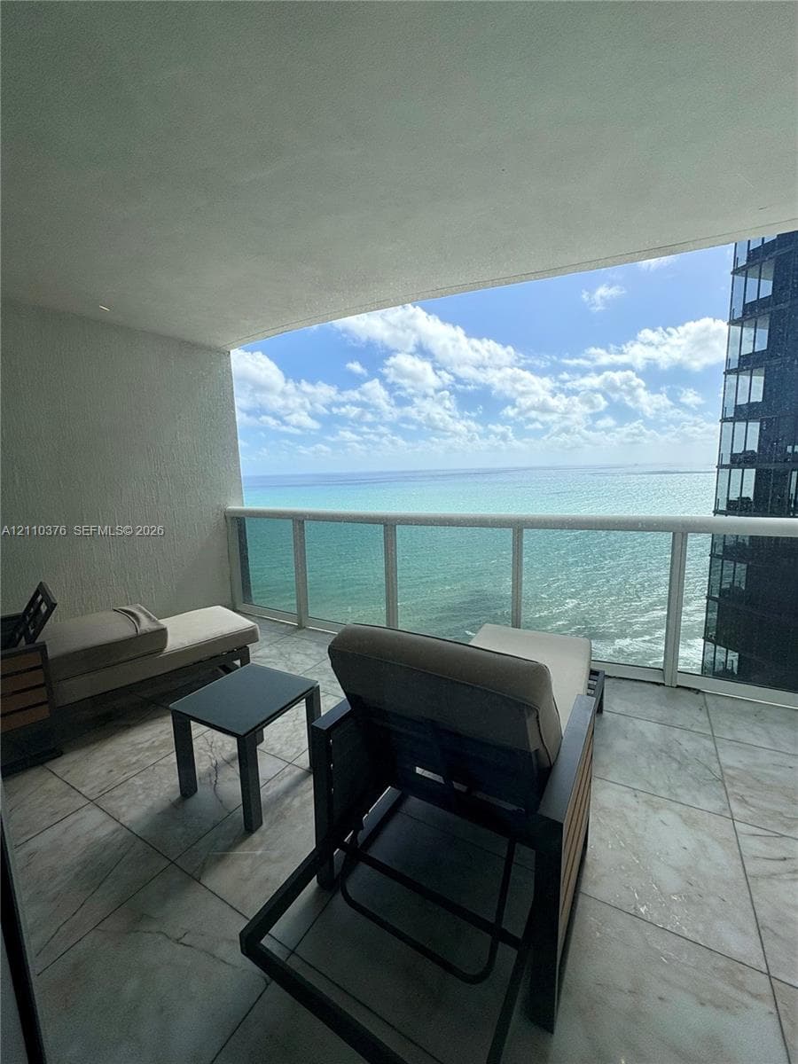 Covered balcony featuring large-format tile flooring and a glass panel railing