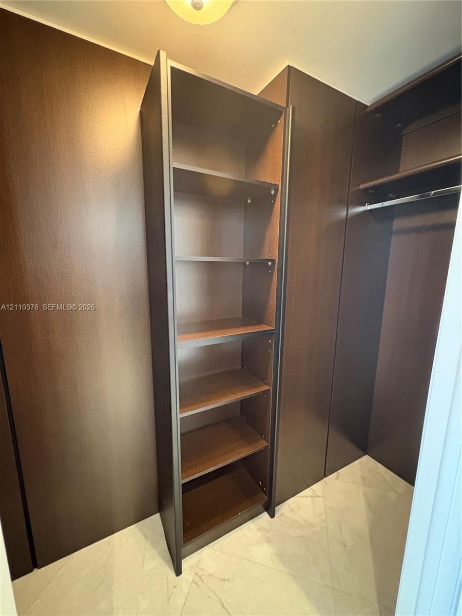 Built-in storage system featuring dark wood-finish cabinetry, adjustable shelving, integrated hanging rods, and large-format tile flooring