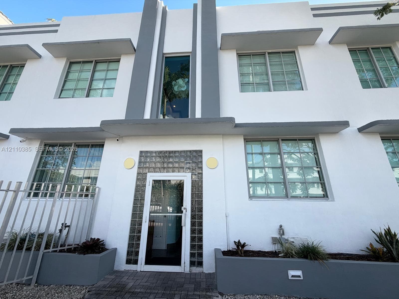 Art Deco facade featuring geometric gray trim, glass block entryway surround, flat roofline, and multi-pane windows