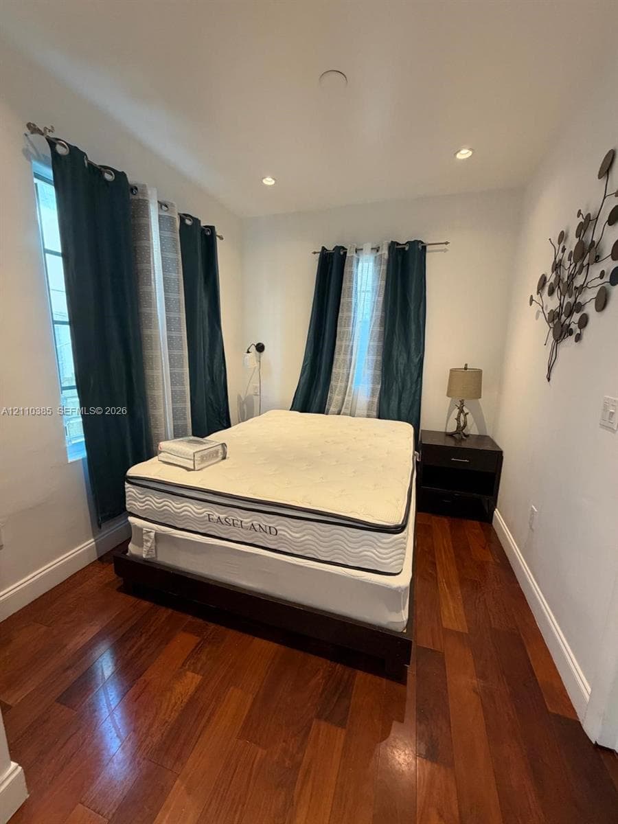 Room featuring wood-finish flooring, recessed lighting, and multiple windows with dual-layer rod-mounted window treatments