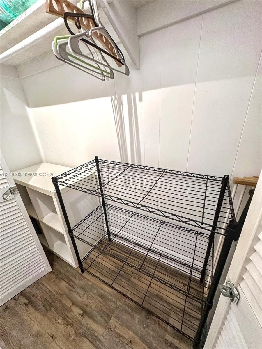 Storage space featuring wood-finish flooring, white paneled wall surfaces, and louvered closet doors