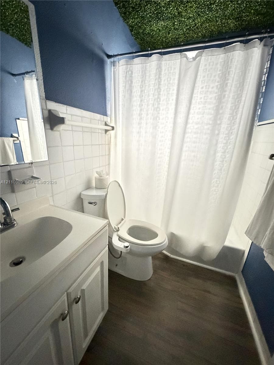 Bathroom featuring a white vanity with integrated basin, wood-finish flooring, white square wall tile, and a textured green ceiling finish