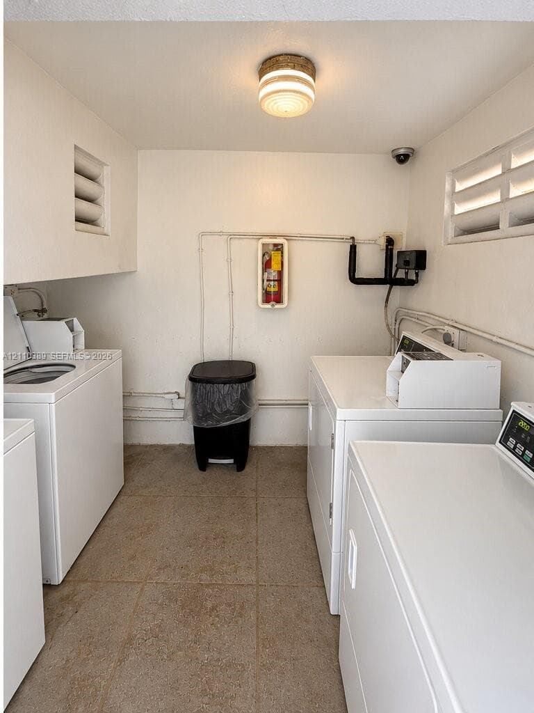 Utility space featuring tiled flooring, flush-mount lighting, wall-mounted fire safety equipment, and dual louvered wall vents