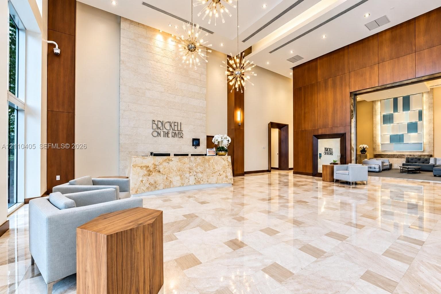 Double-height lobby featuring stone tile flooring, floor-to-ceiling wood paneling, a stone-faced reception desk, and multi-tiered modern pendant lighting