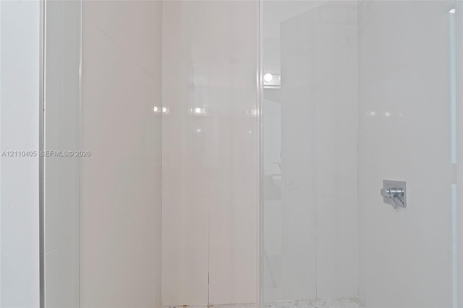 Walk-in shower enclosure with full-height white tile wall surround, glass door, and polished chrome fixtures