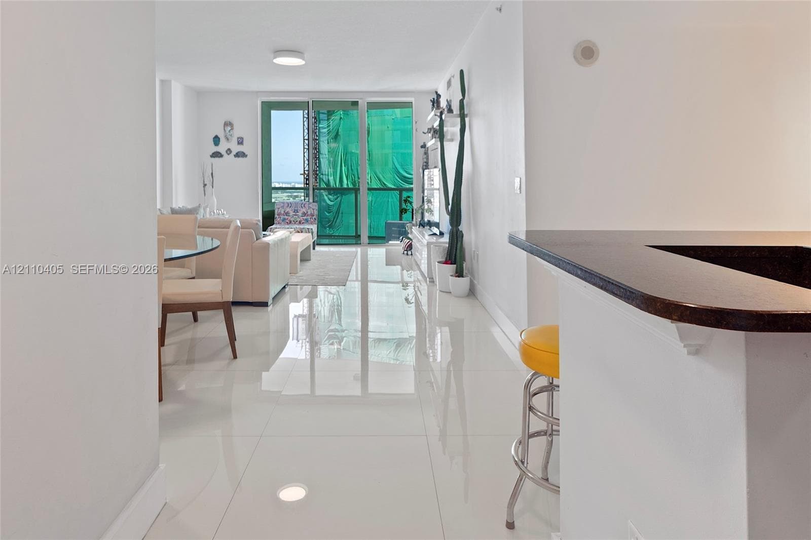 Open-concept interior featuring large-format polished tile flooring, a kitchen breakfast bar with a dark stone countertop, and floor-to-ceiling glass sliding doors